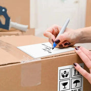 Woman writing with a marker on a white label that is stuck to the top of a cardboard box