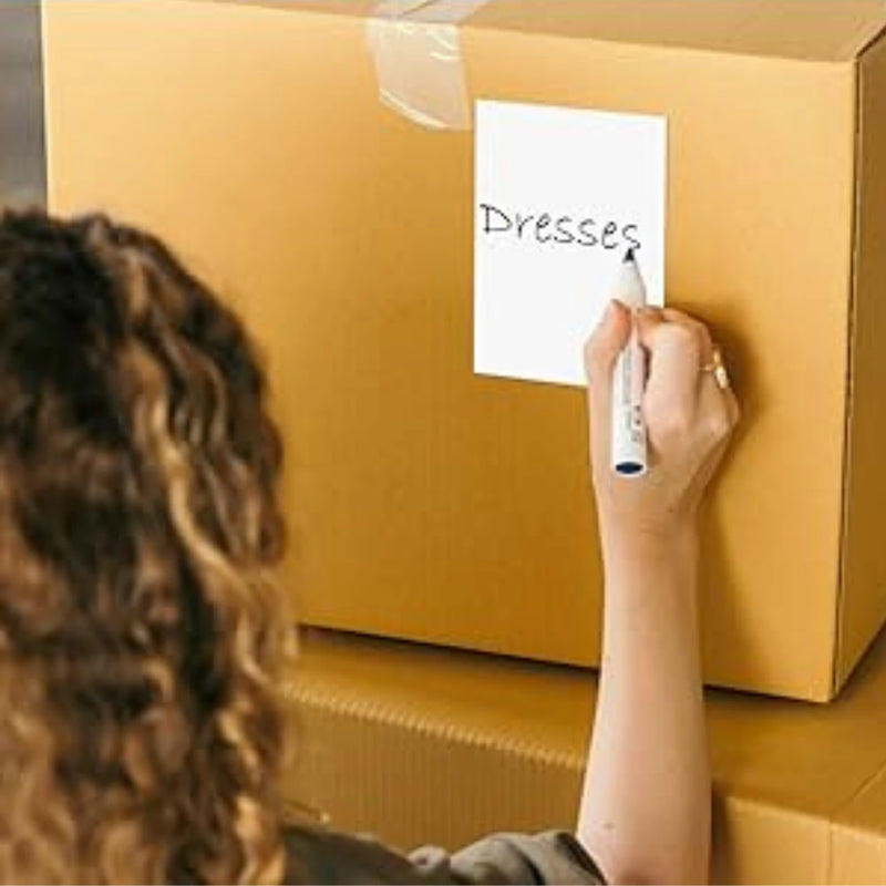 woman writing "dresses" with a black marker on a white label that is stuck to the side of a cardboard box