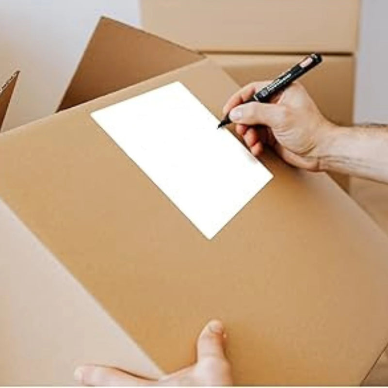 Person about to write with a black marker on a white label that is stuck to the side of a cardboard box