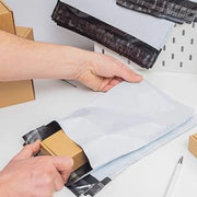Person putting a small cardboard box into a white mailing bag