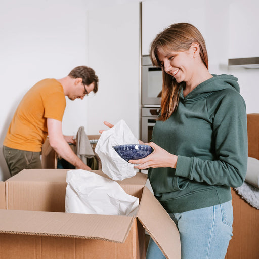 woman using white packing paper to protect a bowl before putting it into a cardboard box