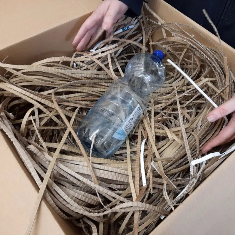 a cardboard box filled with shredded cardboard and an empty 500ml water bottle for size perspective